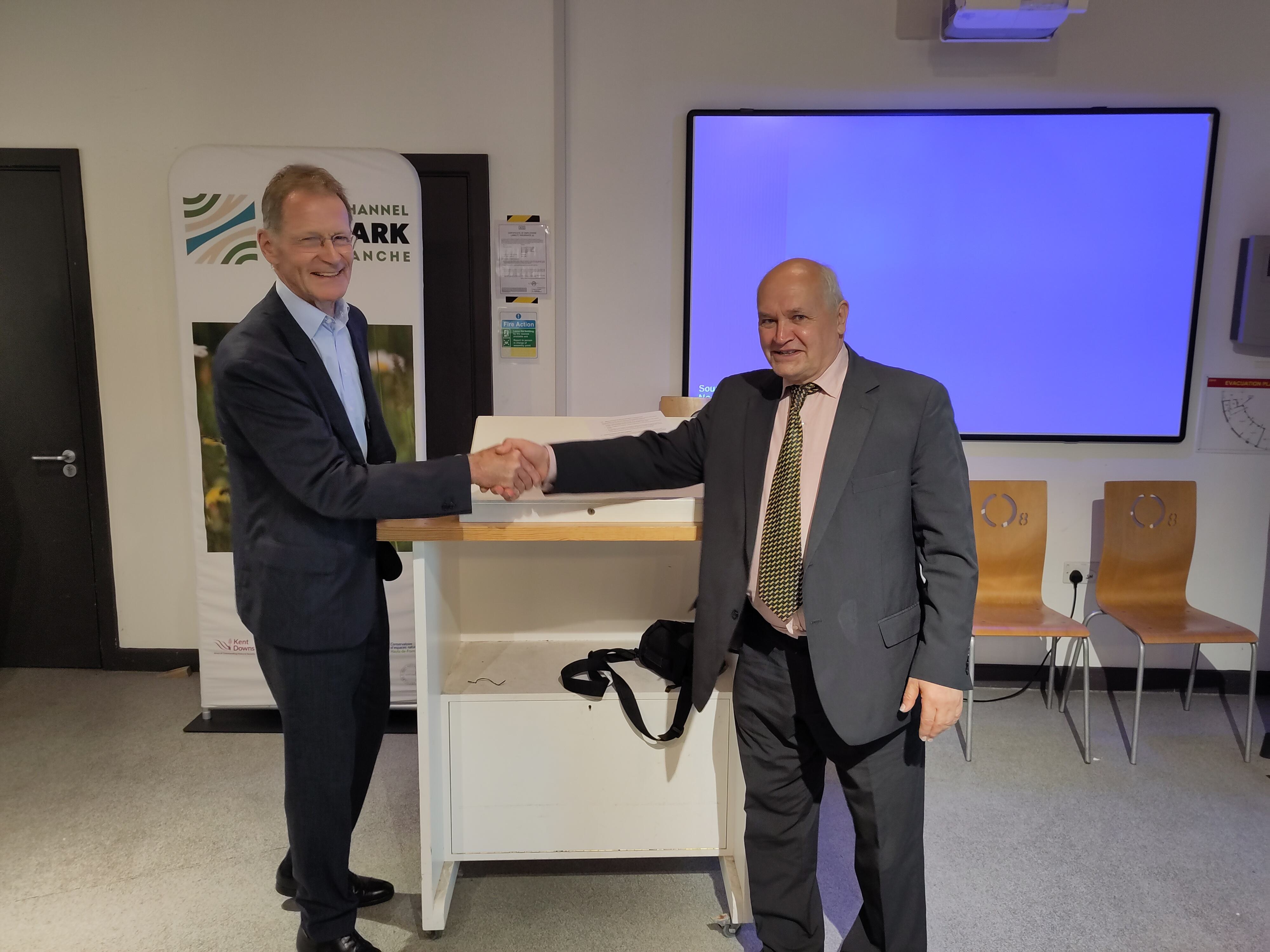 Two men smile and shake hands