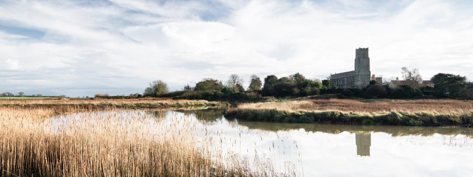 View over and estuary, reeds in the foreground, a church in the background
