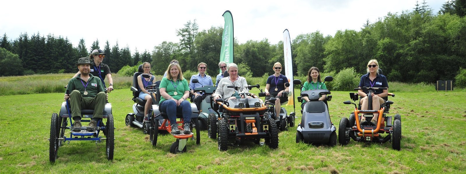 People on trampers, quad bikes and all terrain wheelchairs smile to the camera in a field