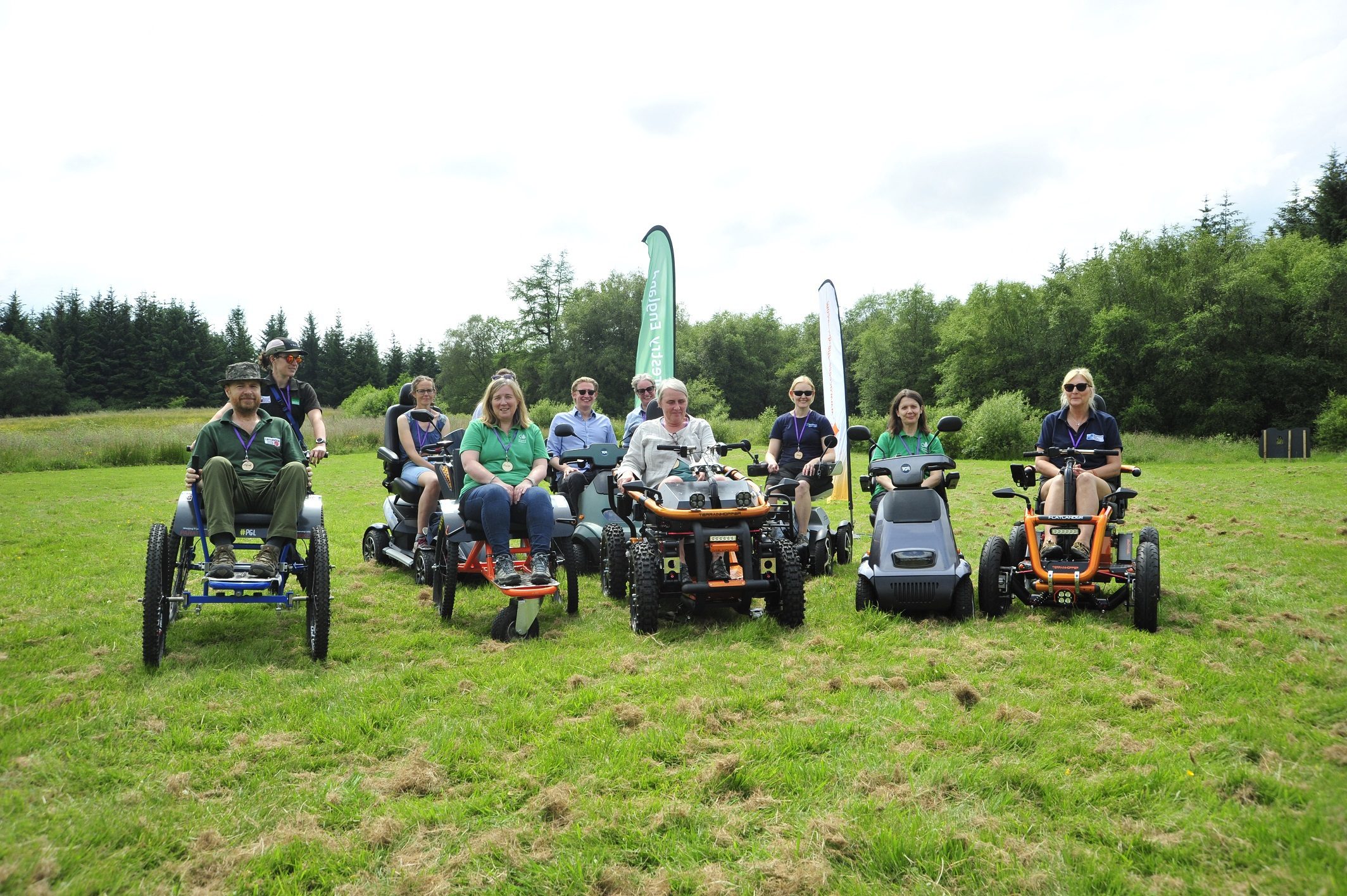 People on trampers, quad bikes and all terrain wheelchairs smile to the camera in a field