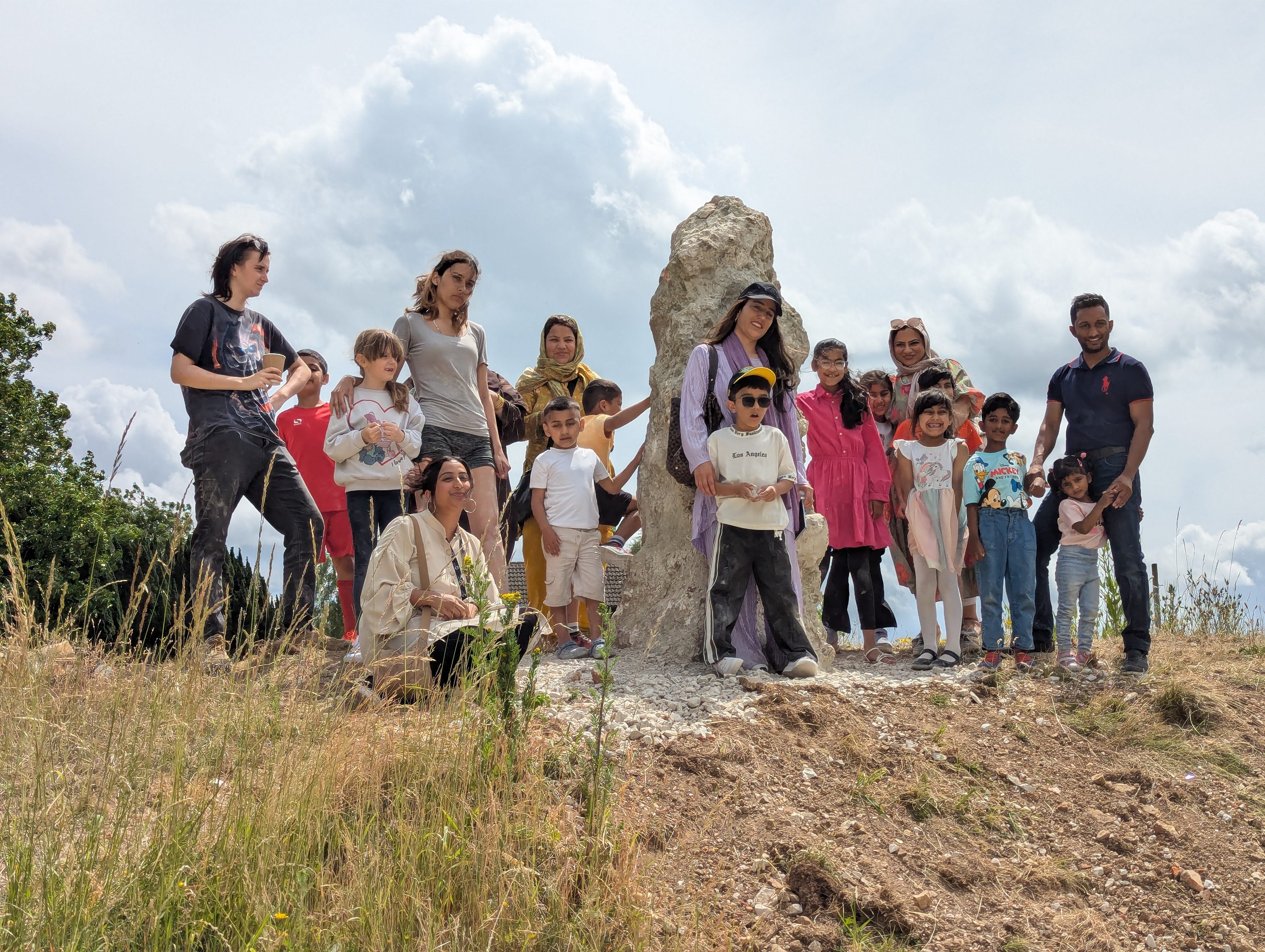 A group of people stand around a standing stone, they are all ages and backgrounds and they look happy