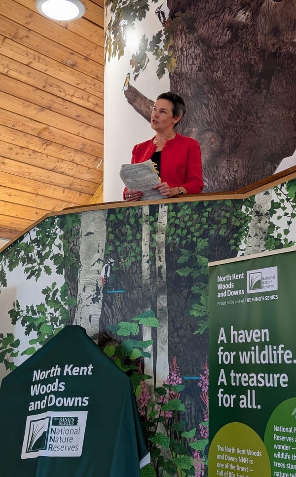 Mary Creagh MP, Minister for Nature is speaking from an elevated landing. She has cropped dark hair and is wearing a red suit jacket.