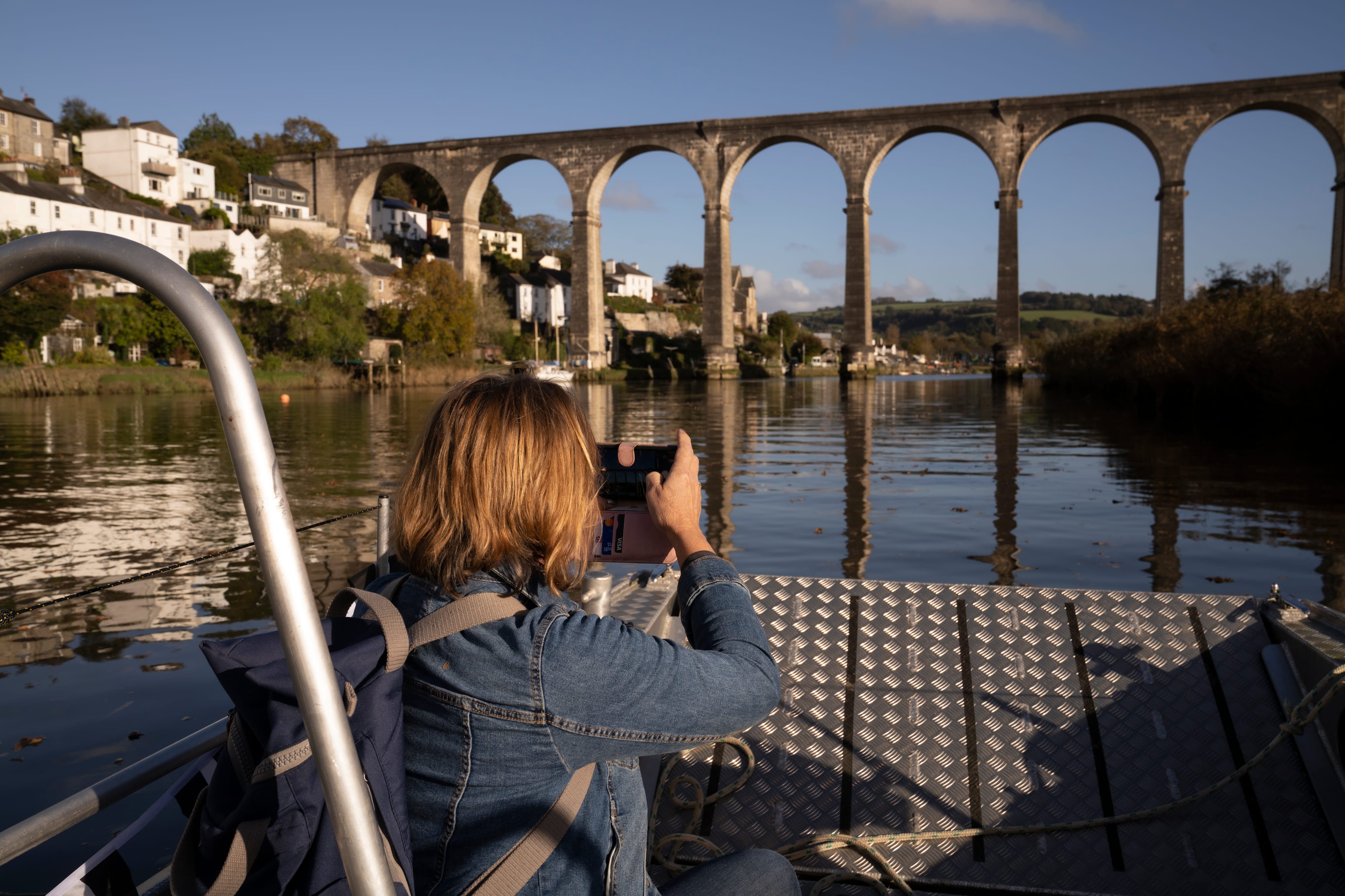 A woman with brown bobbed hair takes a photo of a very tall viaduct. She's aboard a small passenger ferry